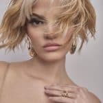 Blonde, tousled wig with layered bangs on a model with gold earrings.